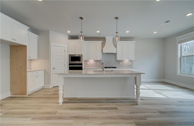 kitchen with premium range hood, a center island with sink, stainless steel microwave, and oven