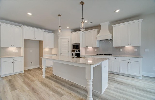 kitchen with white cabinets, custom range hood, stainless steel microwave, black gas cooktop, and a sink