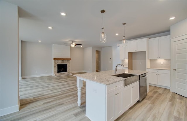 kitchen featuring dishwasher, a kitchen island with sink, white cabinets, and a sink