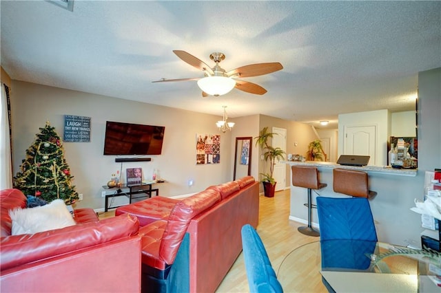 living room with ceiling fan with notable chandelier, a textured ceiling, light wood-style flooring, and baseboards