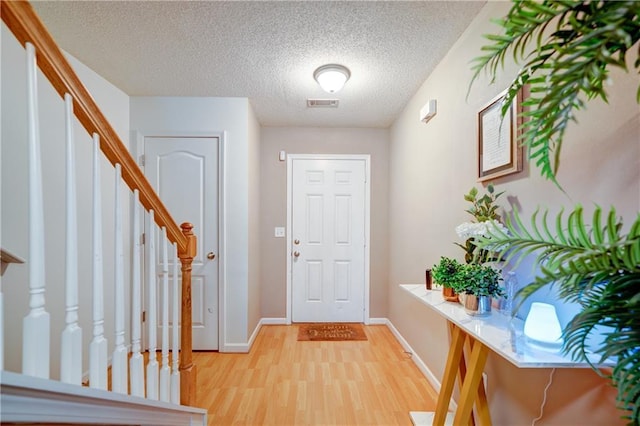 foyer with visible vents, light wood-style floors, a textured ceiling, baseboards, and stairs