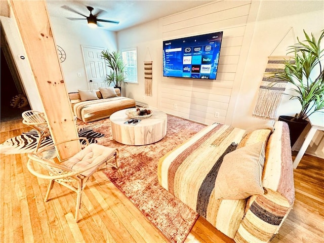 living room featuring ceiling fan, wood-type flooring, and wood walls