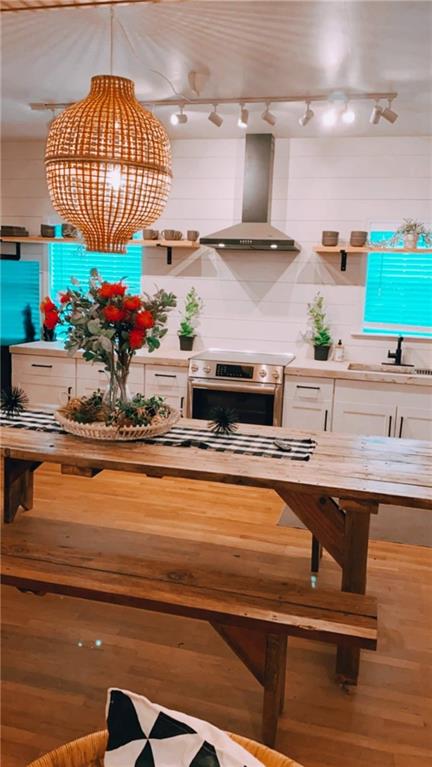 kitchen featuring pendant lighting, white cabinetry, sink, electric range, and wall chimney range hood