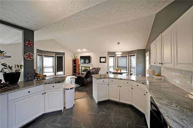 kitchen with open floor plan, lofted ceiling, a peninsula, a glass covered fireplace, and white cabinets