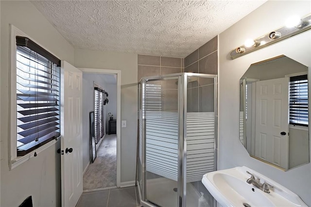 full bath featuring tile patterned floors, a textured ceiling, a stall shower, and a sink