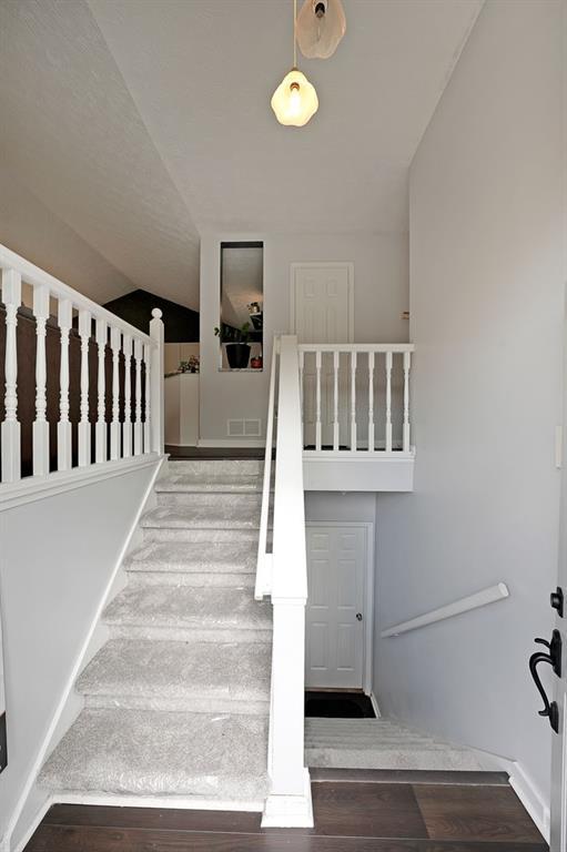 stairs with lofted ceiling, wood finished floors, visible vents, and baseboards