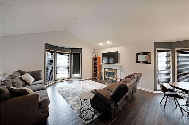 living area featuring a glass covered fireplace, lofted ceiling, baseboards, and dark wood-type flooring