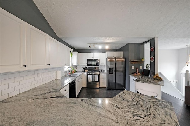 kitchen featuring light stone counters, a sink, decorative backsplash, black appliances, and white cabinetry