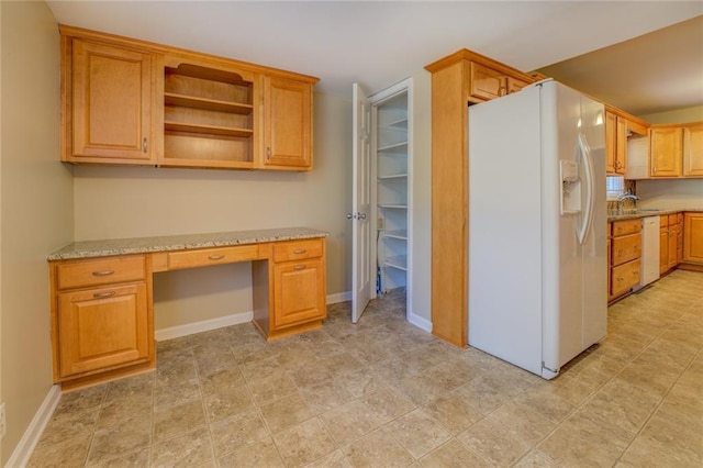 kitchen featuring light stone counters, built in desk, white appliances, and sink