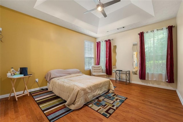 bedroom featuring ceiling fan, a tray ceiling, and wood-type flooring