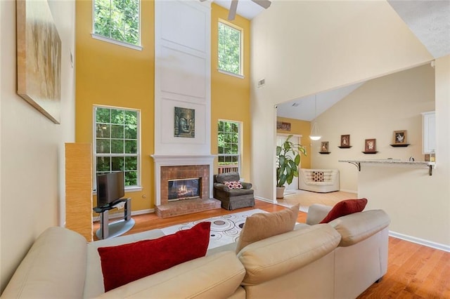 living room featuring a fireplace, high vaulted ceiling, light hardwood / wood-style flooring, and ceiling fan