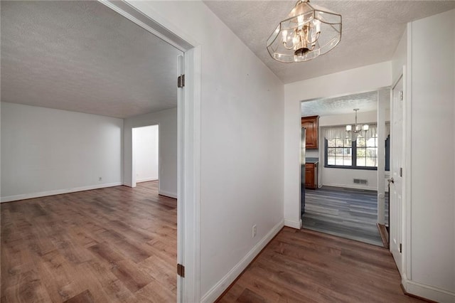 corridor with dark hardwood / wood-style floors, a textured ceiling, and an inviting chandelier