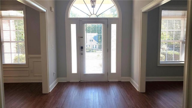 foyer entrance featuring baseboards, a healthy amount of sunlight, dark wood-type flooring, and an inviting chandelier