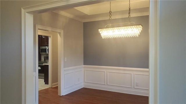unfurnished dining area with an inviting chandelier, crown molding, dark wood-style floors, and wainscoting