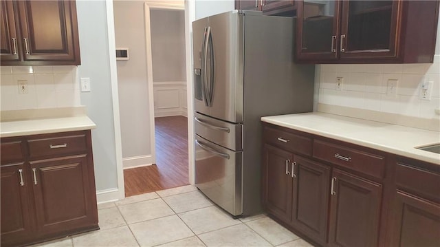 kitchen with tasteful backsplash, glass insert cabinets, light tile patterned floors, stainless steel fridge, and light countertops