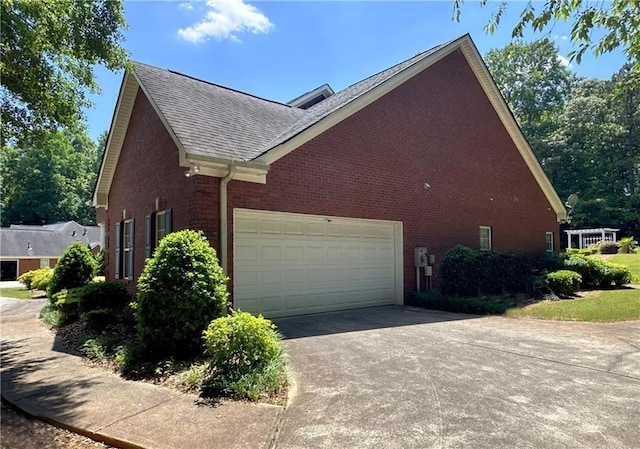 view of side of home with concrete driveway, an attached garage, a shingled roof, and brick siding