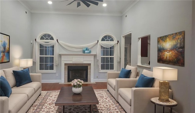 living room featuring wood-type flooring, a tile fireplace, ceiling fan, a high ceiling, and ornamental molding