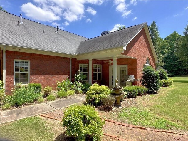rear view of house featuring a chimney, brick siding, a shingled roof, a ceiling fan, and a lawn