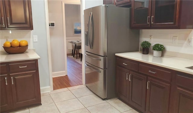 kitchen with light tile patterned floors, tasteful backsplash, glass insert cabinets, light countertops, and stainless steel fridge with ice dispenser