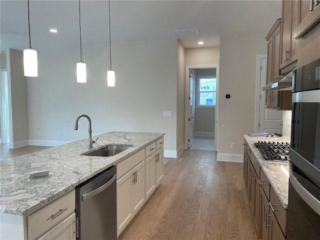 kitchen featuring decorative light fixtures, an island with sink, sink, white cabinets, and stainless steel appliances