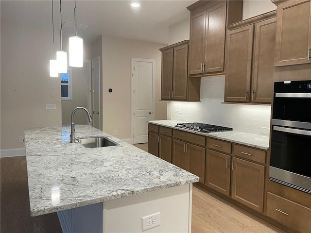 kitchen with a kitchen island with sink, sink, light stone countertops, and appliances with stainless steel finishes