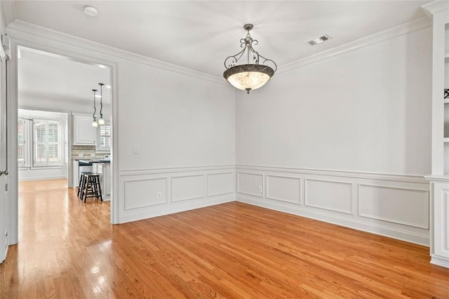 empty room featuring light wood-style flooring, visible vents, and crown molding