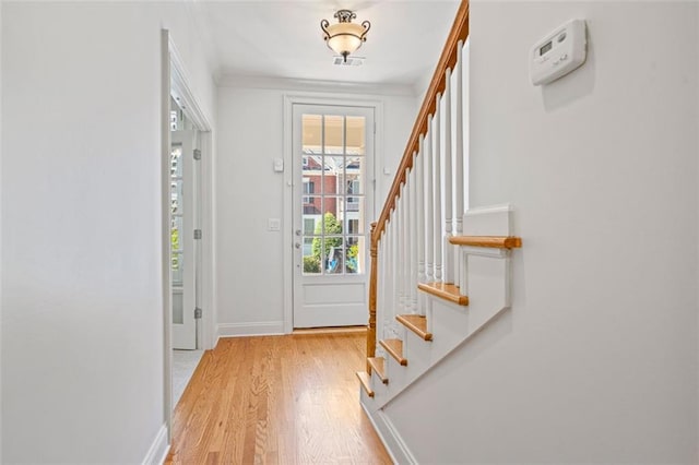 doorway with crown molding, stairway, light wood-style flooring, and baseboards