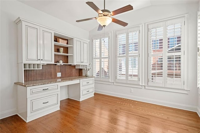 unfurnished office featuring a ceiling fan, light wood-style floors, vaulted ceiling, and built in desk