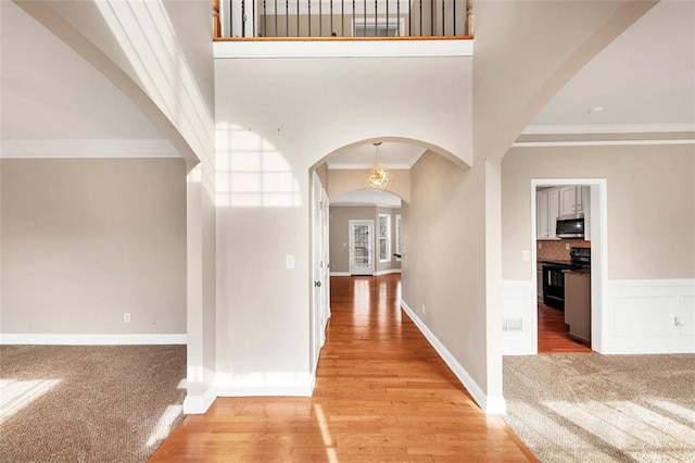 hallway with ornamental molding, a high ceiling, and light wood-type flooring