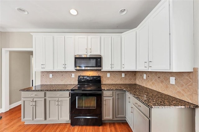 kitchen with black electric range oven, dark stone countertops, white cabinets, and light hardwood / wood-style flooring