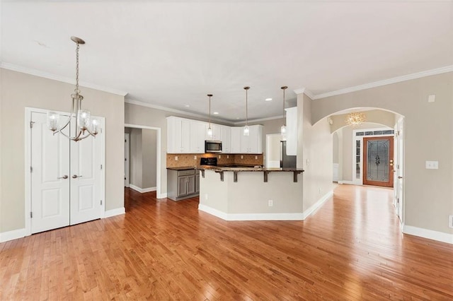 kitchen with white cabinetry, hanging light fixtures, decorative backsplash, kitchen peninsula, and light wood-type flooring