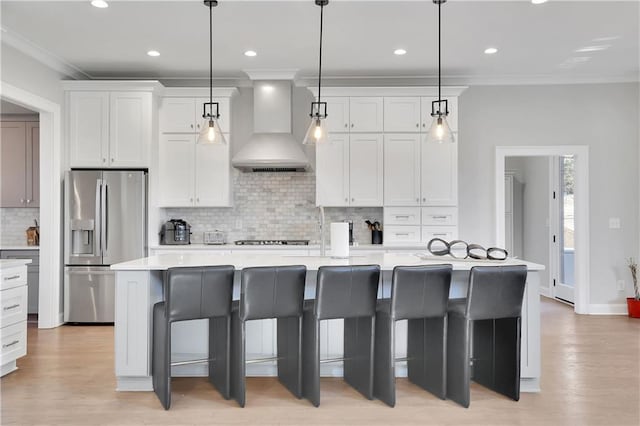 kitchen with light hardwood / wood-style floors, tasteful backsplash, an island with sink, stainless steel appliances, and wall chimney exhaust hood