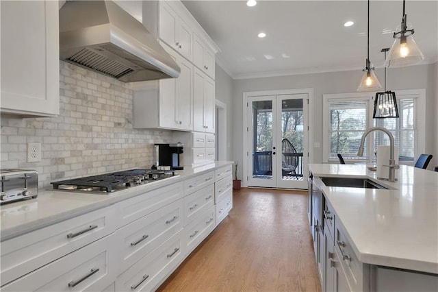 kitchen with crown molding, pendant lighting, wood-type flooring, wall chimney range hood, and sink