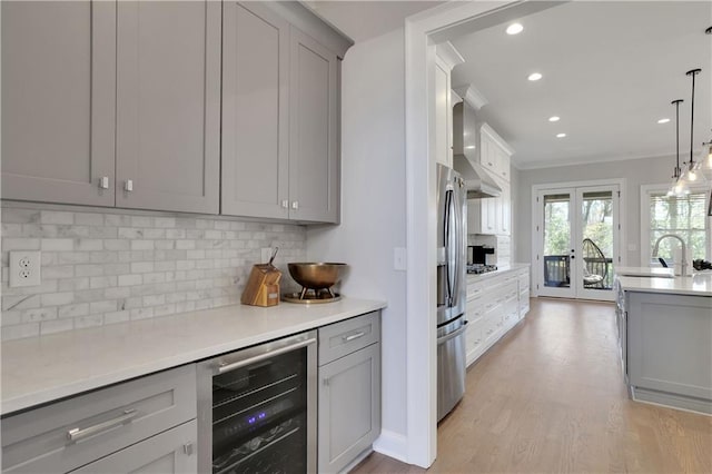 kitchen with wall chimney range hood, light hardwood / wood-style flooring, beverage cooler, pendant lighting, and tasteful backsplash