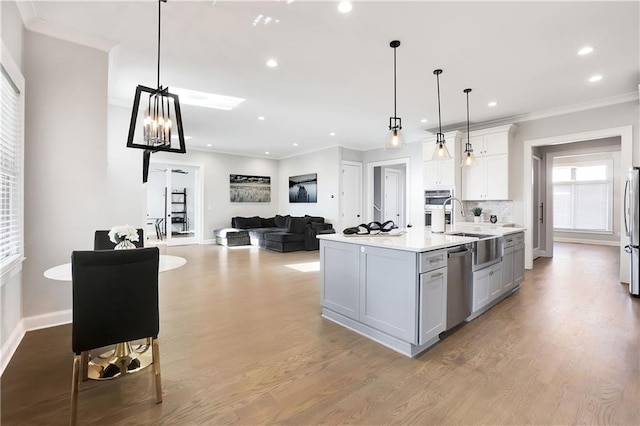 kitchen featuring stainless steel appliances, a center island with sink, crown molding, hardwood / wood-style floors, and pendant lighting