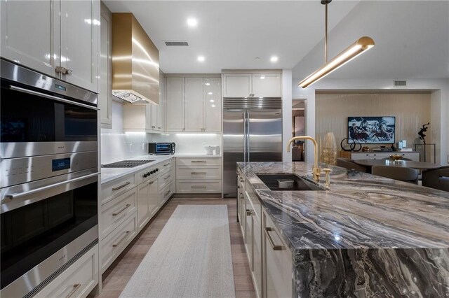 kitchen with floor to ceiling windows, a center island with sink, built in fridge, light stone countertops, and light hardwood / wood-style floors