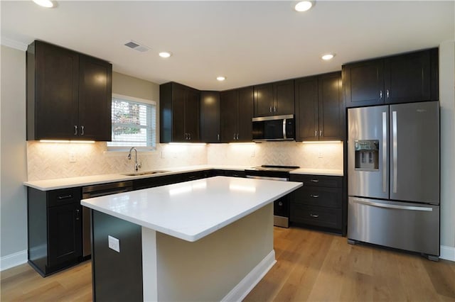 kitchen with appliances with stainless steel finishes, a center island, sink, and light wood-type flooring