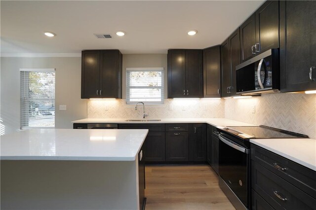 kitchen featuring sink, light hardwood / wood-style flooring, appliances with stainless steel finishes, tasteful backsplash, and a kitchen island