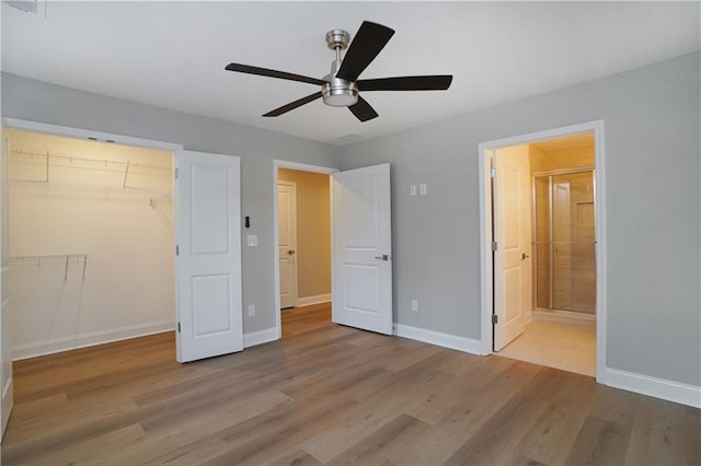 unfurnished bedroom with connected bathroom, a spacious closet, light hardwood / wood-style flooring, a closet, and ceiling fan