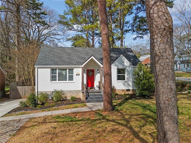 view of front of house with a front lawn, fence, a shingled roof, crawl space, and brick siding