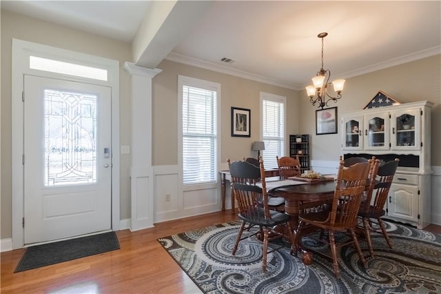 dining room featuring light wood-type flooring, a chandelier, ornamental molding, and decorative columns