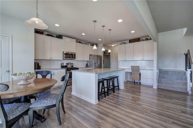 kitchen featuring light wood-type flooring, pendant lighting, stainless steel appliances, a kitchen island with sink, and white cabinets