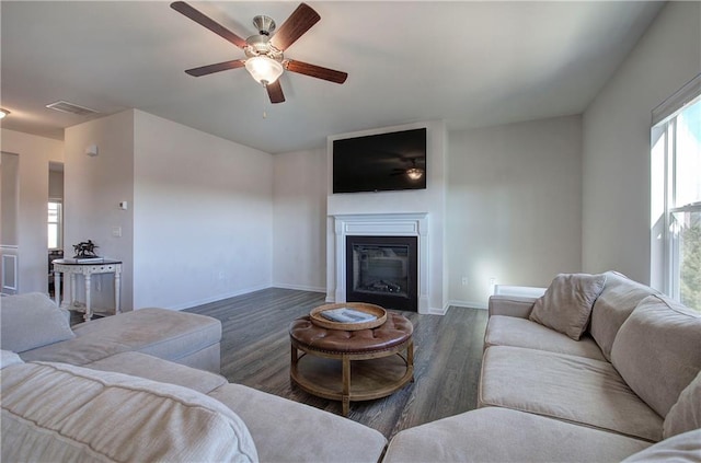 living room with visible vents, a glass covered fireplace, wood finished floors, baseboards, and ceiling fan