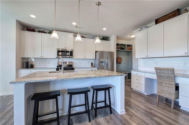 kitchen with dark wood-style floors, a sink, decorative backsplash, built in desk, and appliances with stainless steel finishes