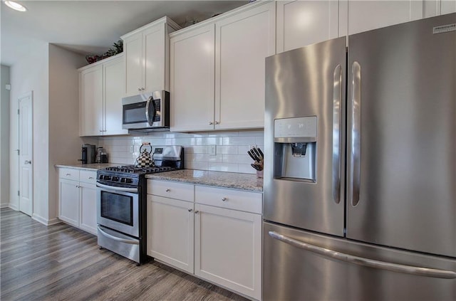 kitchen featuring light stone countertops, wood finished floors, white cabinets, appliances with stainless steel finishes, and backsplash