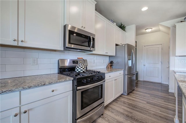 kitchen with stainless steel appliances, white cabinetry, light stone countertops, and light hardwood / wood-style floors