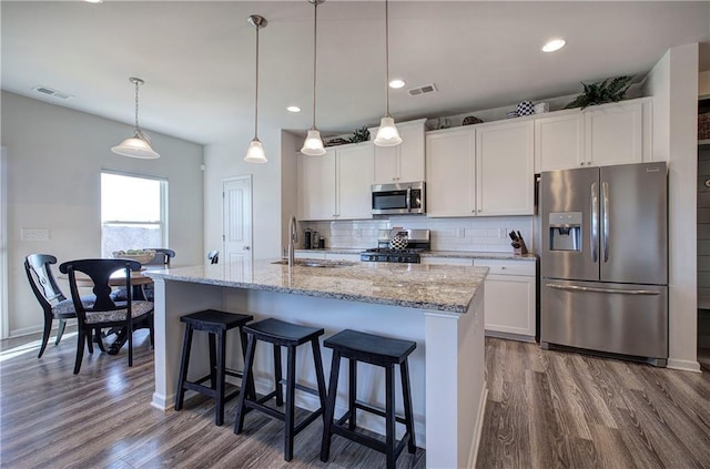 kitchen with pendant lighting, stainless steel appliances, a kitchen island with sink, and white cabinets