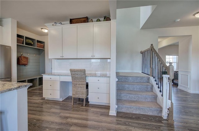 interior space featuring built in desk, wainscoting, a decorative wall, and dark wood-style flooring