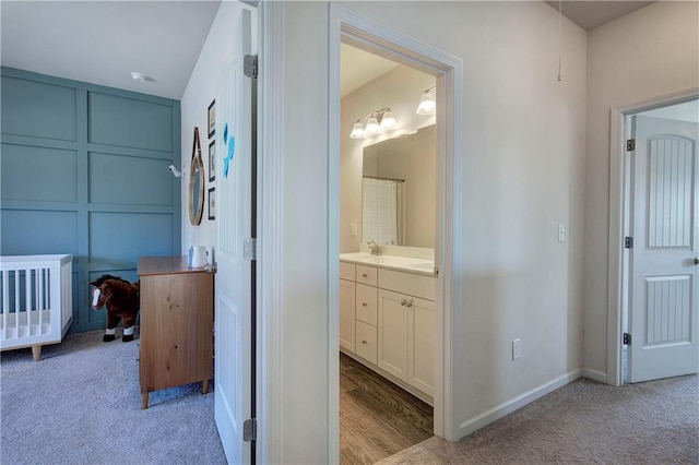 bathroom featuring vanity, a decorative wall, carpet, and baseboards