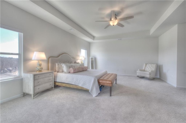 bedroom with a tray ceiling, light colored carpet, and baseboards